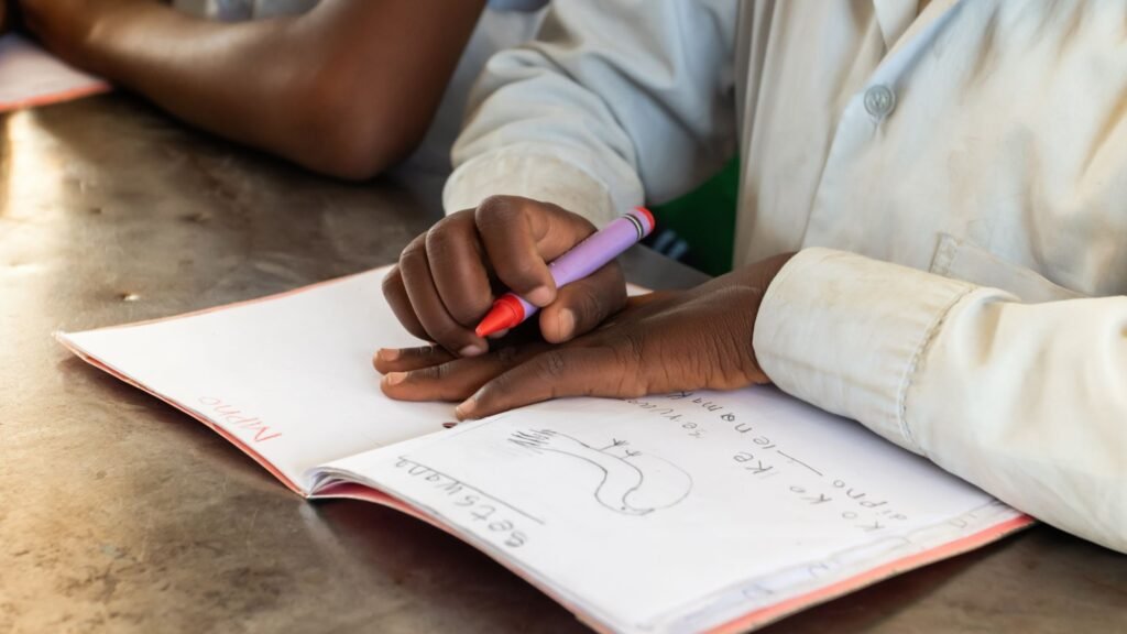 A Ghanaian student focused on writing in a textbook, showing dedication to education and personal growth