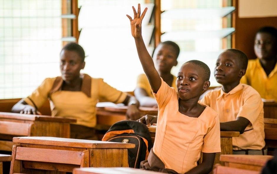 Girl seated in class learning and raising her hand to answer a question