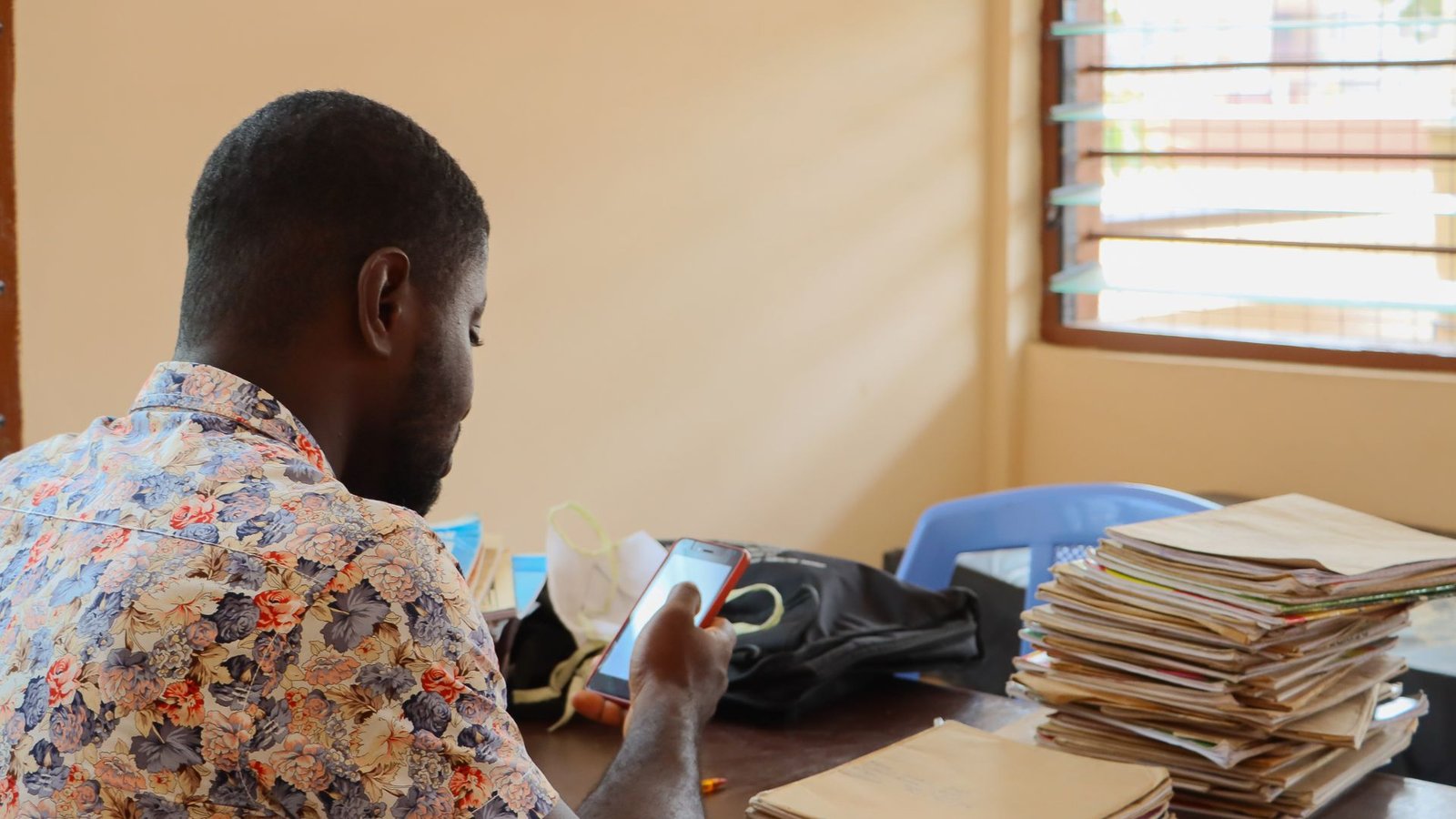 Teacher marking students' work while standing beside a stack of books in a classroom in Ghana.