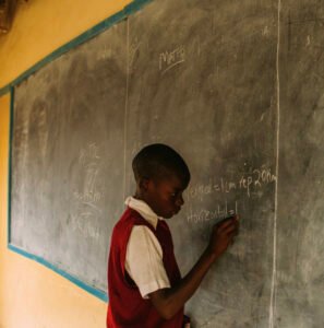 Male student writing on a classroom chalkboard during a lesson in a Ghanaian school.