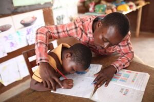Male teacher helping a student practise writing in a classroom.