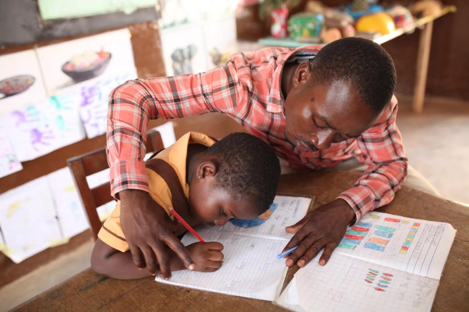 Male teacher helping a student practise writing in a classroom.