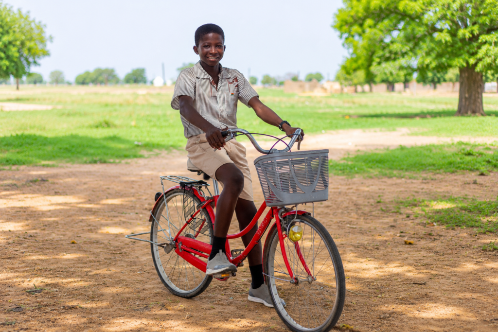 Elisha smiling while sitting on his red bicycle outdoors.
